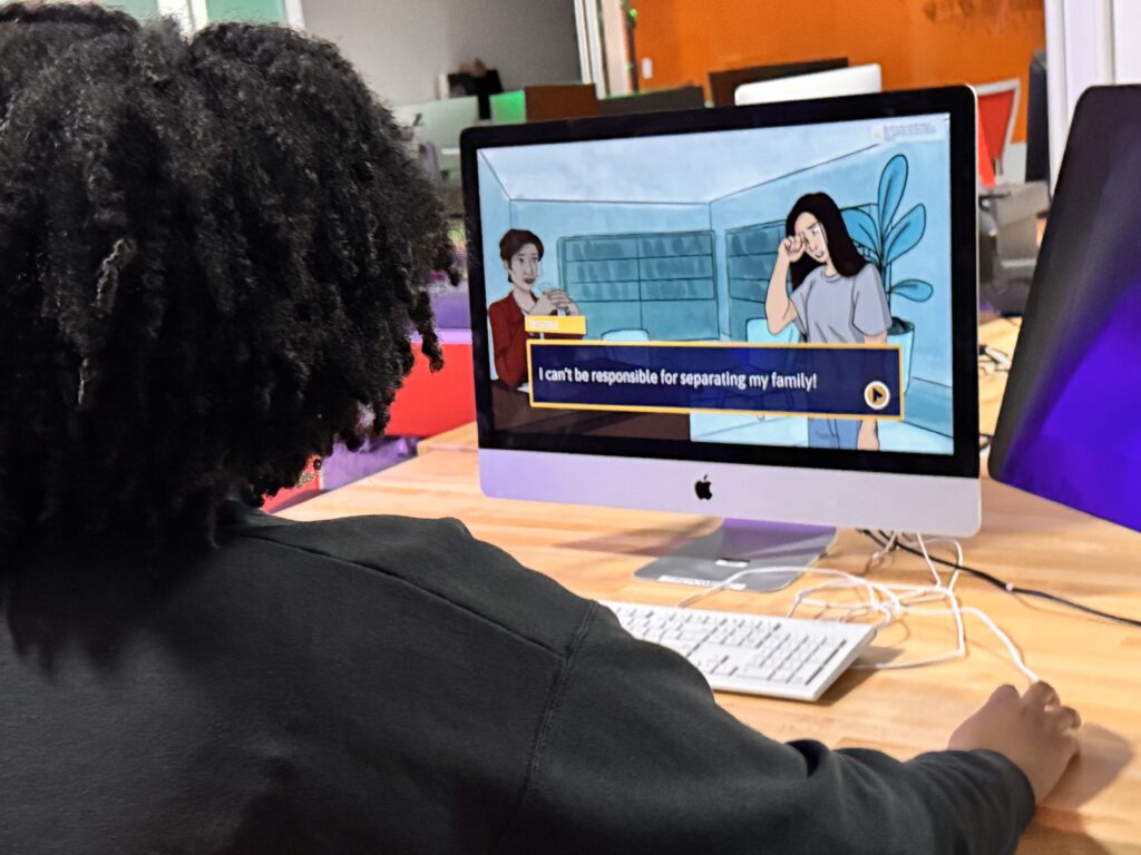 A college student is playing Keys to a DREAM on a Mac computer. On the screen is a flashback scene from August 2000 when Tereza Lee shares her concern about separating her family to her music school director, Ann Monaco.